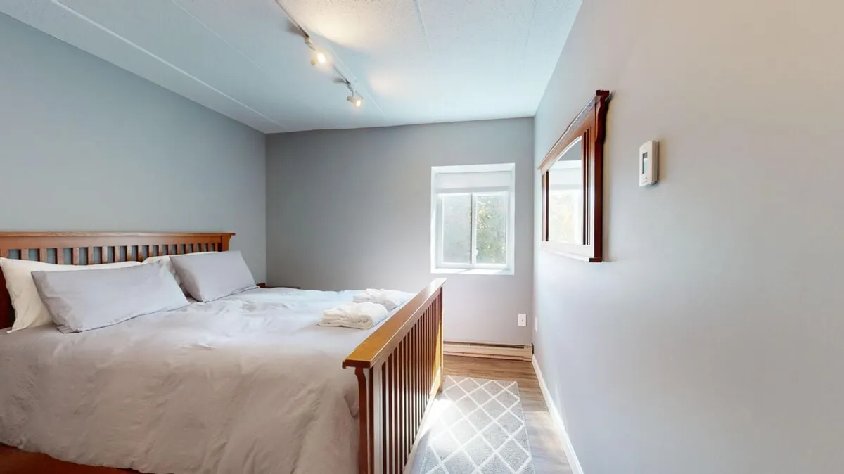 A tranquil bedroom with a bed dressed in white linens sits beside a window that pours in soft natural light. The scene includes a cozy reading nook and a mirror on the wall, creating an inviting space for unwinding after a day of adventure.