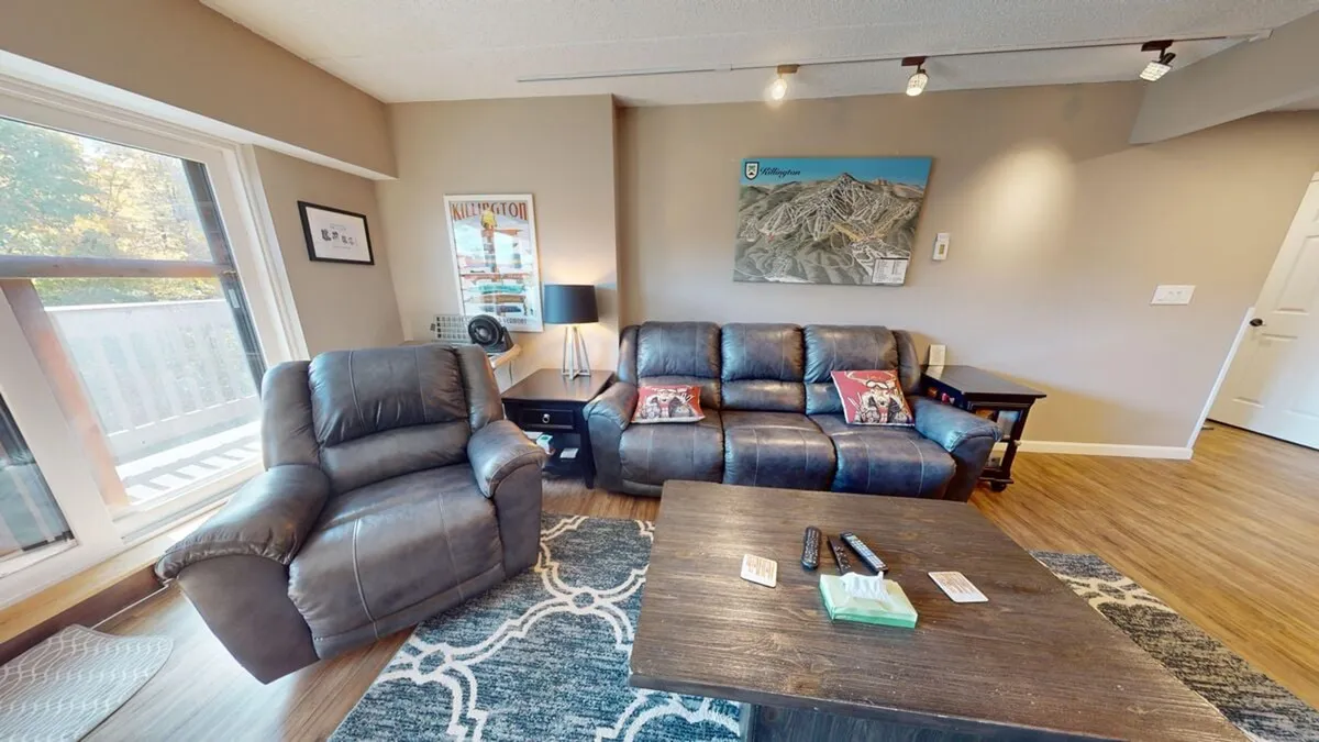 A cozy living room with comfortable seating arranged around a wooden coffee table, complemented by artwork on the walls. The space is designed for relaxation and socializing, with a visible TV, making it ideal for movie nights or playing games.