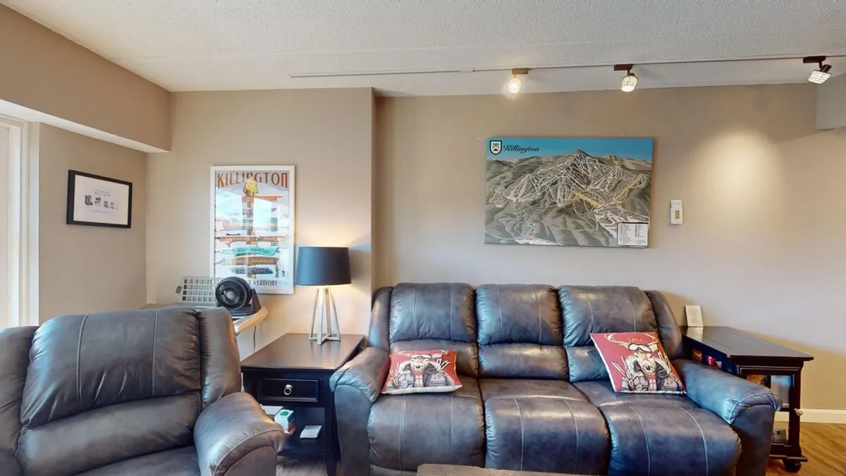 A stylish and comfortable corner with leather sofas, a table lamp, framed artwork, and a detailed map on the wall. Large windows (not fully visible) suggest a connection to outdoor scenery, ideal for relaxing, board games, or watching TV.