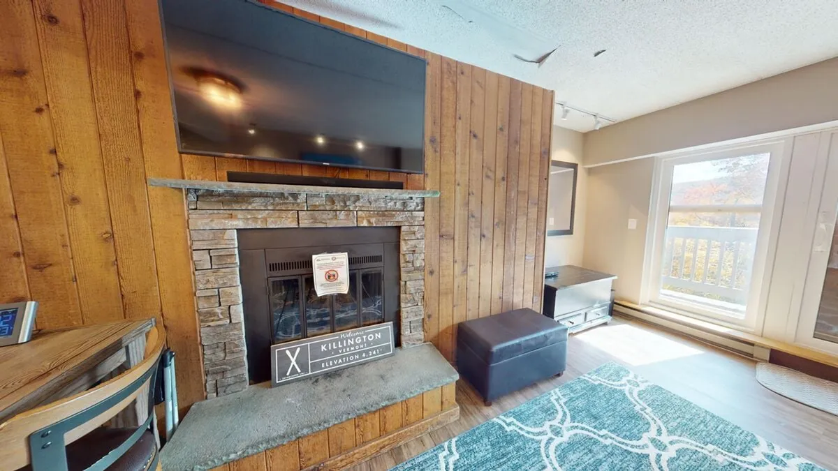 An inviting living area with a cozy fireplace, a television, a plush rug, and a window offering natural light. The scene suggests relaxation and socializing after enjoying resort amenities like the pools or fitness center.