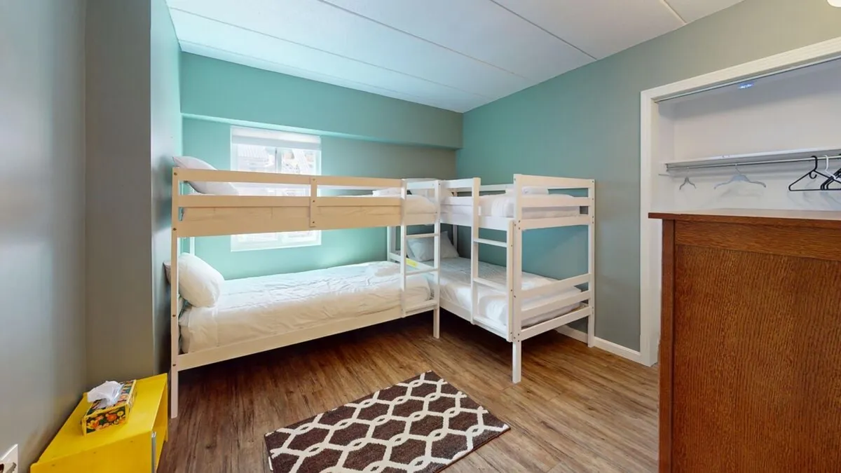 A cheerful room with bunk beds, a window letting in natural light, a playful rug, and bright yellow storage. The environment is playful and inviting, ideal for kids to play, read, and relax after a day spent exploring or swimming.