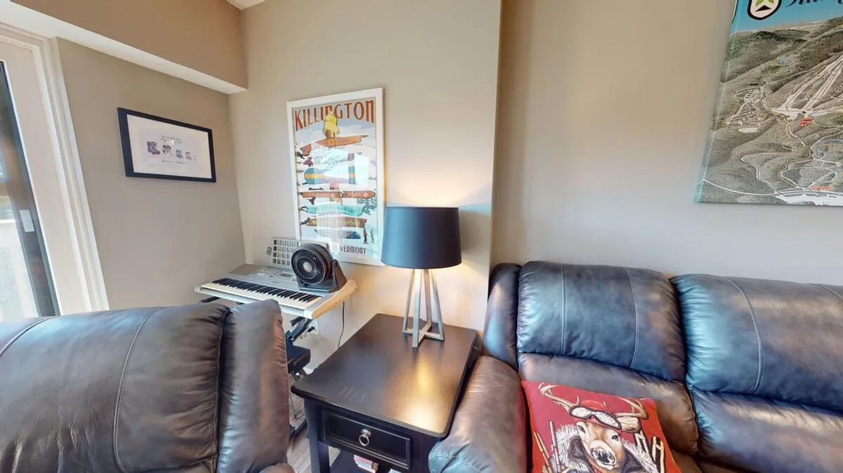 A cozy living area with a leather couch, musical keyboard, table lamp, and a prominent Killington poster on the wall, creating a relaxed and welcoming atmosphere after a day of activity.